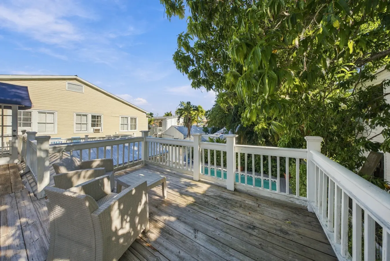 A wooden deck with white railing and outdoor furniture overlooking a pool and building.