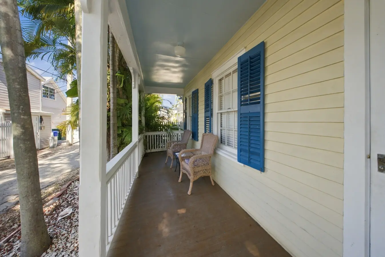 A covered porch with yellow siding, blue shutters, and wicker chairs.