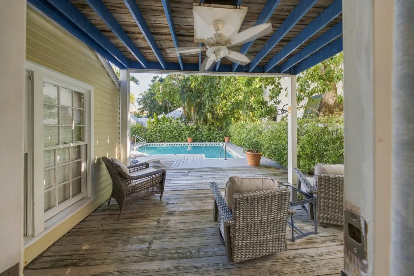 A covered deck with wicker furniture and a pool in the background.