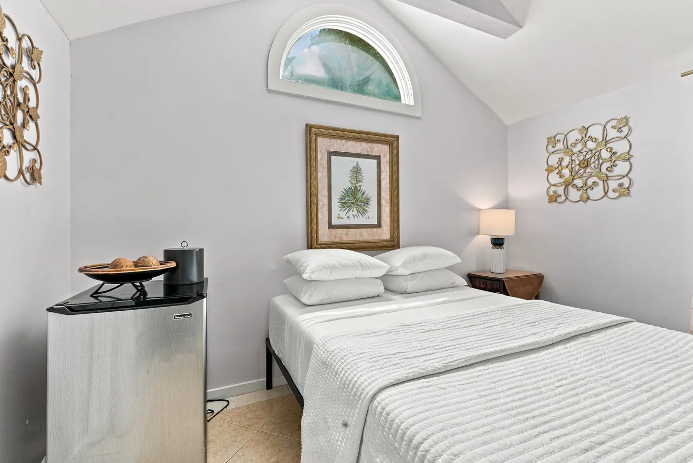A small hotel room with a bed, nightstand, lamp, and mini-fridge.